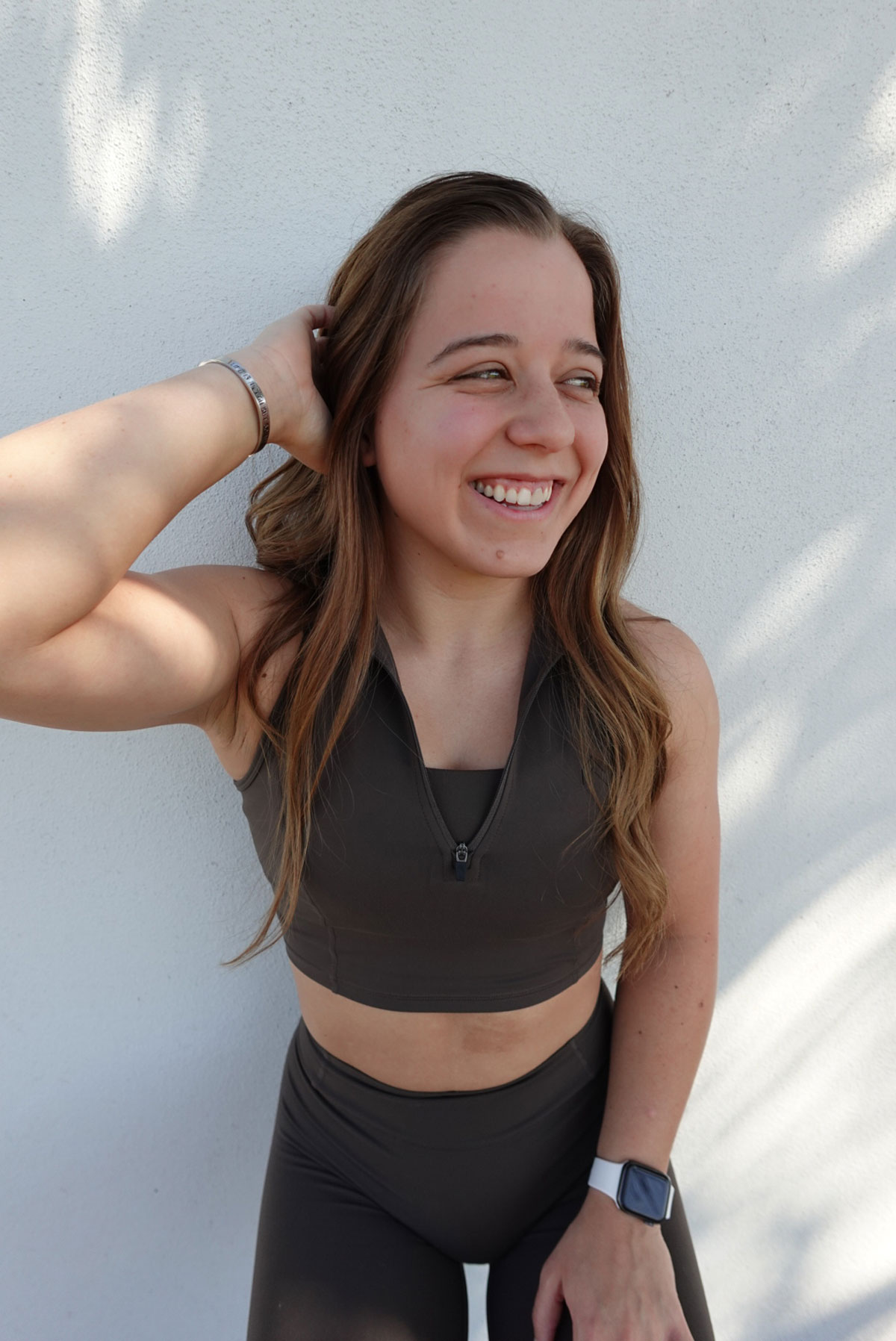 Maddie posing in front of a wall in brown workout clothes.